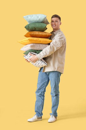 Young man with cushions on yellow backgroundの写真素材