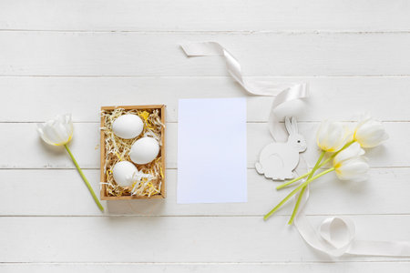Basket with Easter eggs, tulips and blank card on white wooden backgroundの写真素材