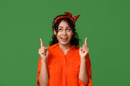Stylish African-American woman pointing at something on green backgroundの写真素材