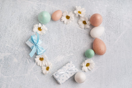 Stylish wreath with gift boxes, Easter eggs and chamomiles on light background