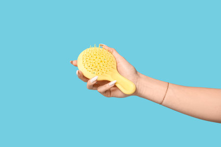 Female hand with yellow hair brush on blue backgroundの写真素材