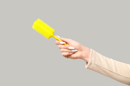 Female hand with yellow hair brush on gray backgroundの写真素材
