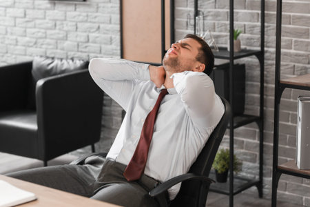 Businessman suffering from neck pain in office at nightの写真素材