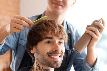 Male hairdresser spraying client's hair in barbershop, closeupの写真素材