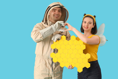Male beekeeper with paper honeycombs and woman in bee costume making heart gesture on blue...