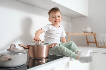 Little boy opening lid pot on electric stove in kitchen. Child at riskの写真素材