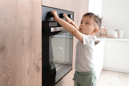 Little boy opening electric oven in kitchen. Child at riskの写真素材