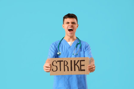Protesting male doctor holding placard with word STRIKE on blue backgroundの写真素材