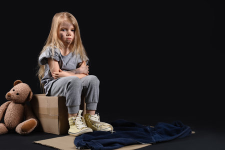 Homeless little girl sitting on cardboard box against dark backgroundの写真素材