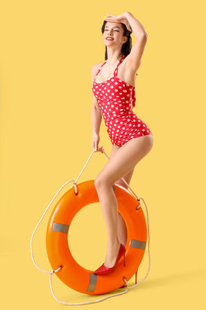 Beautiful pin-up lifeguard with ring buoy on yellow backgroundの写真素材