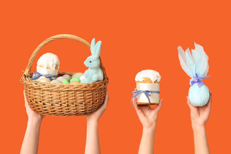 Female hands holding basket with eggs, Easter cake and gift on orange backgroundの写真素材