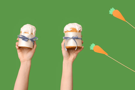 Female hands holding Easter cakes with decor on green background