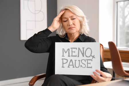 Mature businesswoman holding paper with the word MENOPAUSE in officeの写真素材