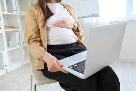 Beautiful pregnant businesswoman with laptop sitting in officeの写真素材