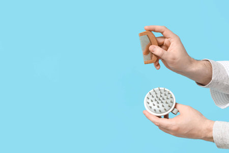 Male hands with hair scalp massager and comb on blue backgroundの写真素材