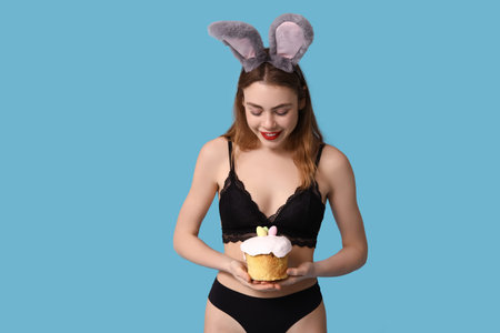 Sexy smiling young woman in bunny ears with Easter cake on blue background