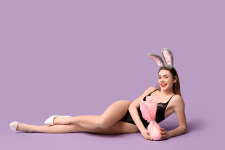 Sexy smiling young woman in bunny ears with Easter gift lying on lilac backgroundの写真素材