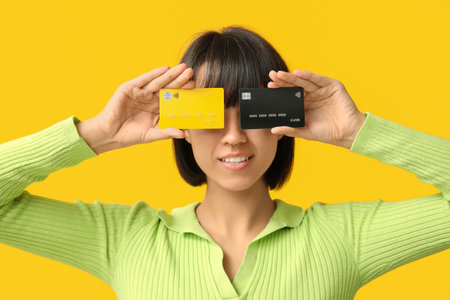 Beautiful young woman with credit cards on yellow backgroundの写真素材