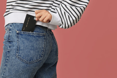 Young woman with credit card in jeans pocket on pink background, closeupの写真素材