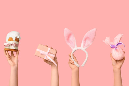 Female hands holding Easter cake with gift box, bunny ears and gift on pink backgroundの写真素材