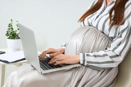 Young pregnant businesswoman working with laptop near light wall, closeupの写真素材