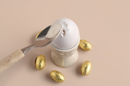 Teaspoon breaking egg in polka dot holder and chocolate candies on beige background, closeup. Easter concept.の写真素材