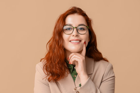 Smiling young redhead woman in eyeglasses on beige backgroundの写真素材