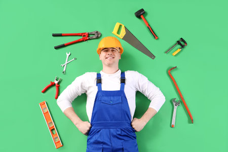 Male builder with work tools on green background, top view