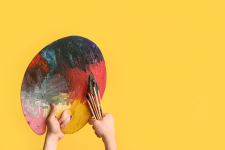 Female hands with artist's tools on yellow backgroundの写真素材