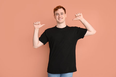 Young man pointing at his black t-shirt on beige backgroundの写真素材