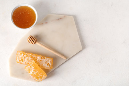 Board with bowl of sweet honey and combs on light backgroundの写真素材