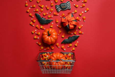 Shopping basket with tasty candy corns, cookies for Halloween and pumpkins on red background