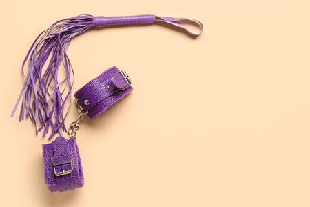 Handcuffs and whip from sex shop on beige background