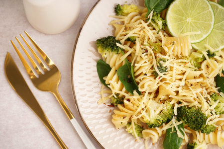 Delicious fusilli pasta with broccoli, cheese and lime slices in plate on light background, closeupの写真素材