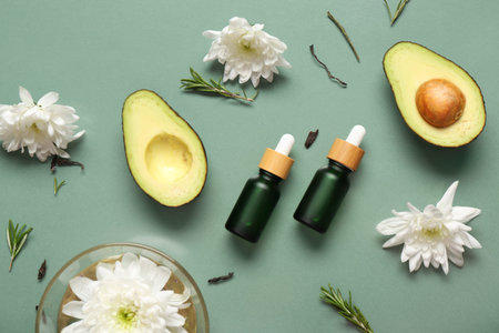 Composition with bottles of essential oil, avocado and flowers on color background