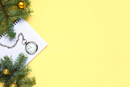 Pocket watch with notebook and Christmas tree branches on yellow background