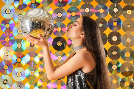Stylish young woman with disco ball against compact disksの写真素材