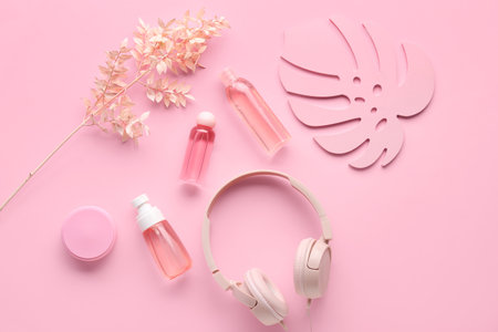 Composition with modern headphones, bottles of cosmetic products and leaf on pink backgroundの写真素材