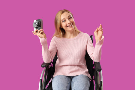 Mature woman in wheelchair with photo camera on violet backgroundの写真素材