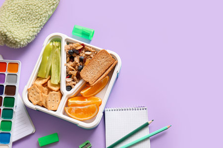 Lunchbox with delicious food and different stationery on lilac backgroundの写真素材