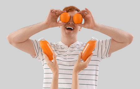Young man with oranges and bottles of juice on light backgroundの写真素材