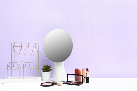 Different makeup products, mirror and houseplant on dressing table near purple wall in roomの写真素材