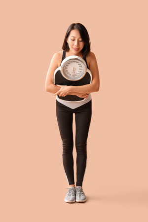 Beautiful young Asian woman with scales on beige background. Weight loss conceptの写真素材