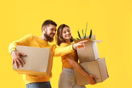 Happy couple in love with moving boxes on yellow backgroundの写真素材