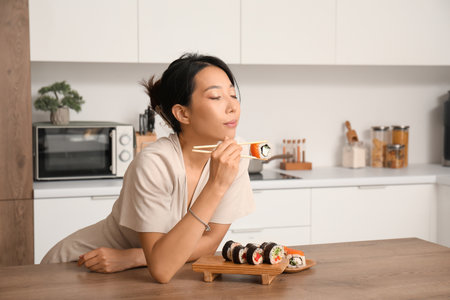 Beautiful young Asian woman with tasty sushi rolls in kitchenの写真素材