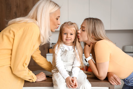 Cute little girl with her mother and granny kissing in kitchenの写真素材