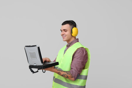 Young male engineer with laptop on gray background