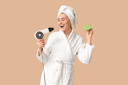 Happy young woman with hair scalp massager and hairdryer on brown backgroundの写真素材