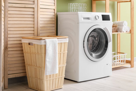 Modern washing machine with basket, shelving unit and dressing screen near green wall. Interior of home laundry roomの写真素材