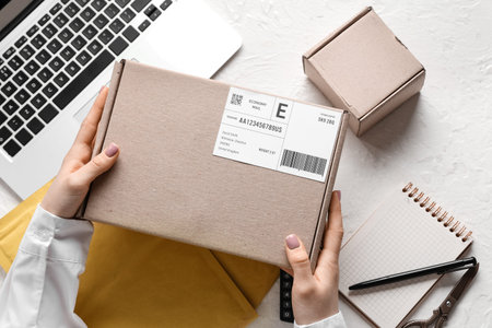 Female hands holding cardboard package at white table with laptop and envelopesの写真素材